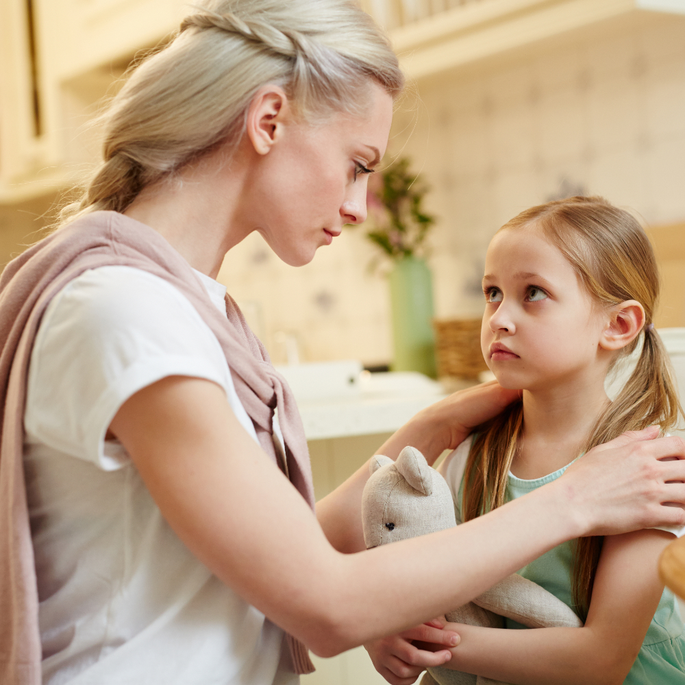 Young sad woman looking at her little daughter during talk in the kitchen